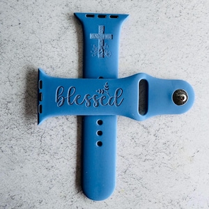 May include: A blue silicone Apple Watch band with a cross and floral design on one side and the word "blessed" on the other side.