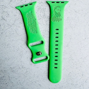 May include: Two green silicone watch bands with different designs. One band features a graphic design and the other band features a portrait of a man with the text "Cashman".