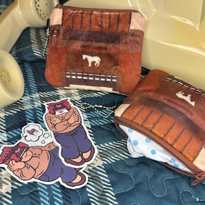 May include: Two brown zippered pouches with a repeating design of a building and a white horse. One pouch is open, revealing a blue and white polka dot pattern. Also, two stickers of a cartoon man.