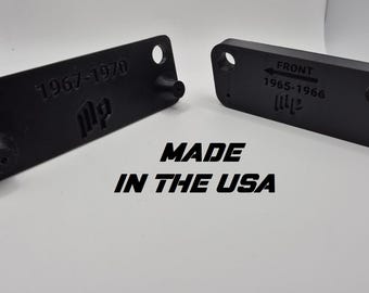May include: Two black rectangular parts with rounded corners, each featuring holes and protruding elements. One part is labeled "1967-1970" and the other "1965-1966 FRONT". The text "MADE IN THE USA" is displayed below.