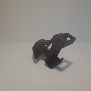 May include: A black plastic phone stand with a simple design. The stand is designed to hold a phone upright.