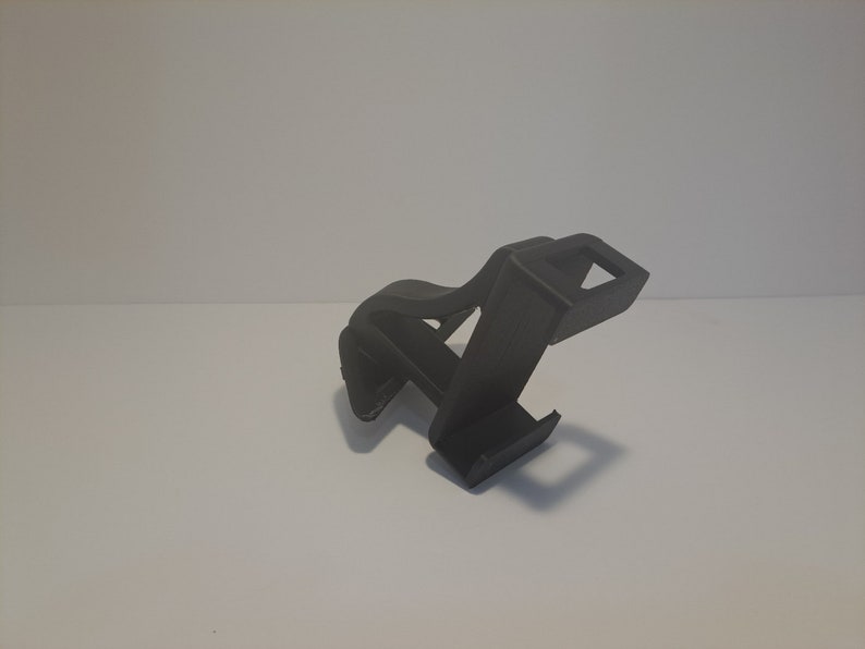 May include: A black plastic phone stand with a simple design. The stand is designed to hold a phone upright.