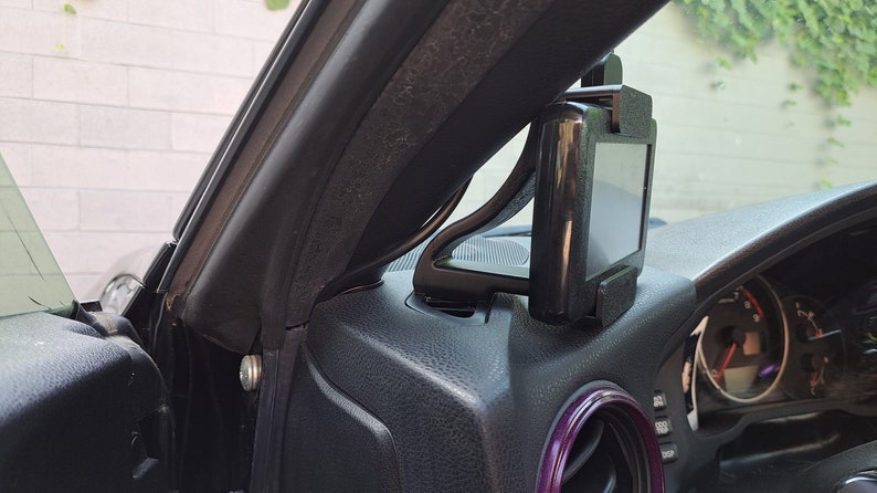 May include: A black car phone mount attached to the dashboard of a car. The mount is designed to hold a phone in a vertical position.