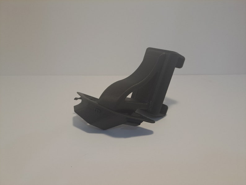 May include: A black plastic phone holder with a swivel design. The holder is designed to be mounted on a desk or table.