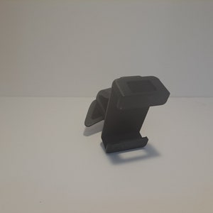 May include: A black plastic phone holder with a clip on the back. The holder is designed to be attached to a car vent.