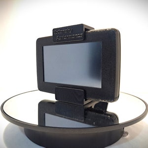 May include: A black device with a screen and the text "McCrathy Performance" on the top. The device is sitting on a black circular stand with a mirrored surface.