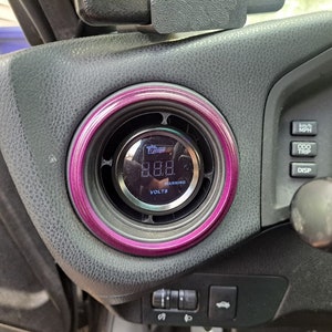 May include: A close-up of a car's dashboard with a pink and black gauge that reads "8.88" volts. The gauge is labeled "VOLTS" and has a "WARNING" indicator. The dashboard also has buttons labeled "KM/H MPH", "ODO TRIP", and "DISP".