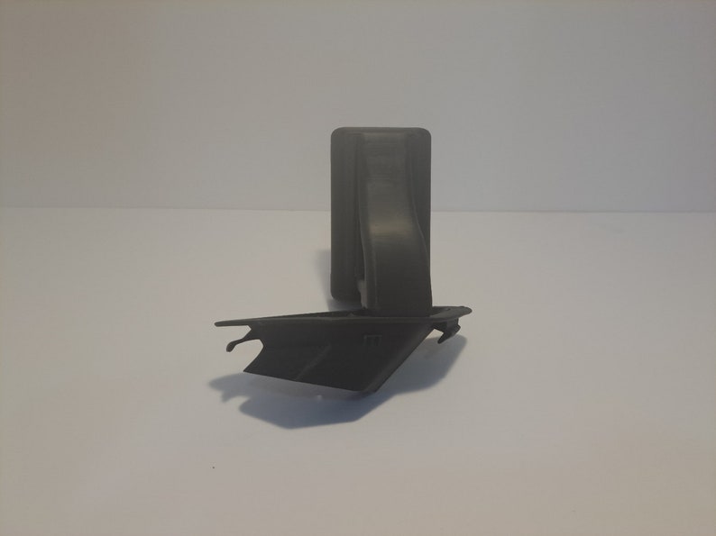 May include: A black plastic object with a rectangular base and a curved arm extending from the top. The object is designed to hold a phone or other device.
