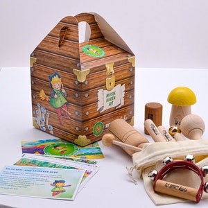 Könnte beinhalten: Eine Holzkiste gefüllt mit Musikinstrumenten für Kinder. Das Set beinhaltet ein Xylophon, eine Tamburin, ein Satz Glöckchen und einen Holzpilz mit gelber Kappe. Die Kiste ist mit einer Comic-Hexe und den Worten "Musik Hexen Set" verziert.
