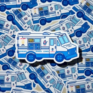 May include: A white ice cream truck with blue accents and a red roof. The truck has a sign that says "Sundae's" and "Shakes Cones".