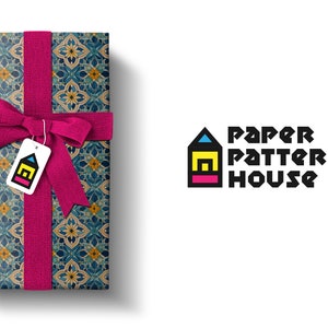 Op de afbeelding: Een cadeaudoos ingepakt in blauw, geel en bruin gepatroneerd papier met een roze lint en een label met de tekst "Paper Pattern House".