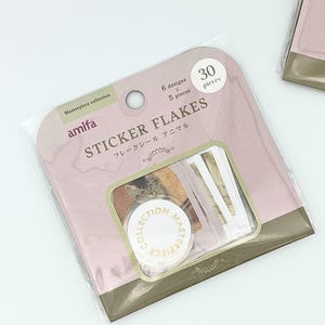 以下が含まれることがあります： 「Masterpiece collection amifa STICKER FLAKES」と書かれた、モーヴ色とオリーブグリーンのパッケージに入った30枚のフレークシール。透明な窓からは、動物の画像が描かれた小さなシールと、「COLLECTION MASTERPIECE」という文字が入った円形のシールが見えます。