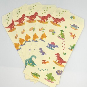 以下が含まれることがあります： カラフルな恐竜のイラストで飾られた、薄い黄色の封筒の束。封筒には、赤、オレンジ、緑、紫色のさまざまな恐竜が描かれており、緑色の足跡やその他の装飾要素も含まれています。封筒は扇形に配置されています。