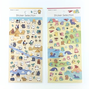 以下が含まれることがあります： 「Sticker Selection」および「Made in Japan」と記された2枚の縦型ステッカーシート。左側のシートにはピラミッドなどのエジプトをテーマにした小さなキャラクターが描かれています。右側のシートには、様々な活動をしているカラフルな恐竜のキャラクターが描かれています。