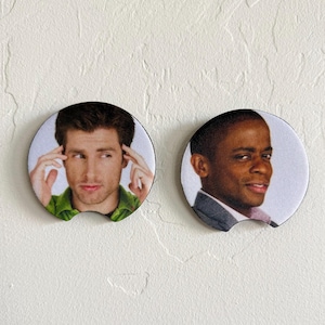 Op de afbeelding: Twee ronde onderzetters voor in de bekerhouder van een auto met fotoprints van twee verschillende mannen. De linker onderzetter toont een man met bruin haar in een groen shirt, de rechter een man met kort donker haar in een grijs colbert.