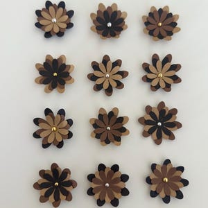 Peut inclure: Douze fleurs en papier superposées dans des tons de marron, beige et noir, disposées en grille. Chaque fleur a un centre métallique, avec des accents dorés ou argentés. Les fleurs sont sur fond blanc.