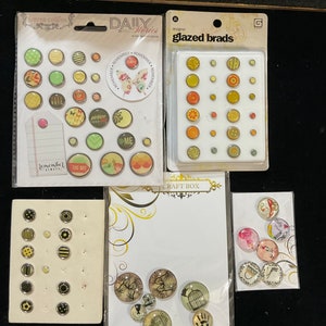 May include: Assortment of colorful, patterned, and decorative craft embellishments.  The embellishments are in various shapes and sizes, including circles, squares, and butterflies.  The embellishments are packaged in clear plastic bags with labels that say "Daily Stories" and "Glazed Brads".