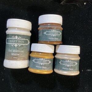 May include: Four small jars of craft supplies with white lids. The jars are labeled "Gel Medium Matte", "Velvet Paste", and "Stencil Paste". The jars are various colors, including gold and off-white.