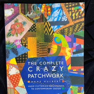 May include: A book titled "THE COMPLETE CRAZY PATCHWORK" by Anne Hulbert. The cover features a vibrant patchwork design with various fabric patterns and colors, including orange, blue, yellow, and green. The subtitle reads "FROM VICTORIAN BEGINNINGS TO CONTEMPORARY DESIGN."