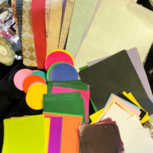 May include: A collection of colorful paper sheets and circular cutouts in various sizes and hues. The assortment includes shades of pink, orange, yellow, green, purple, and blue, along with patterned and textured paper. Ideal for crafting and scrapbooking projects.