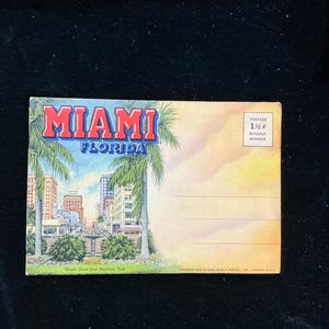 May include: Vintage postcard featuring a colorful illustration of a street scene in Miami, Florida. The postcard has the text "Miami Florida" in large, bold letters at the top and "Flagler Street from Bayfront Park" at the bottom. The postcard also has a postage stamp in the upper right corner that says "Postage 1 1/2¢ Without Message".