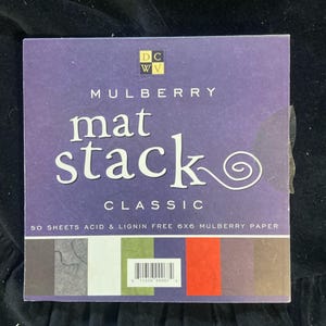 May include: A square DCWV Mulberry Mat Stack Classic paper pad featuring 50 sheets of 6x6 inch acid and lignin-free mulberry paper. The purple cover displays the product name and a color palette of gray, white, green, blue, red, and brown.