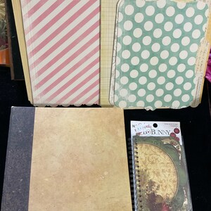 May include: A set of decorative paper sheets with various patterns, including pink and white stripes, green with white polka dots, and a beige sheet with a floral design. The papers are arranged in a stack on a black surface. There is also a small, brown, spiral-bound notebook with a floral design on the cover.