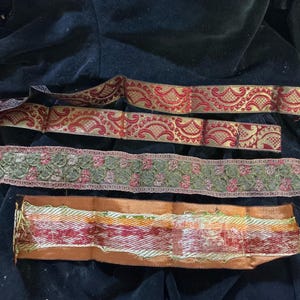 May include: Assortment of decorative ribbons in various designs and colors. Includes red and gold patterned ribbons, a green floral ribbon, and a multi-colored ribbon with orange edges. Ideal for crafts and embellishments.