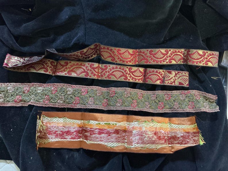 May include: Assortment of decorative ribbons in various designs and colors. Includes red and gold patterned ribbons, a green floral ribbon, and a multi-colored ribbon with orange edges. Ideal for crafts and embellishments.