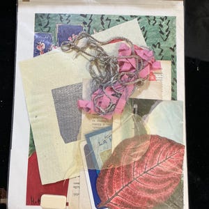 May include: A collage of paper scraps, including a red leaf, a piece of pink ribbon, and a piece of gray fabric. The collage is on a white background.