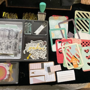 May include: A set of scrapbooking supplies including stamps, die cuts, patterned paper, and stickers. The stamps feature phrases like "Home is where the heart is" and "You are my sunshine". The die cuts are in the shape of hearts, arrows, and stars. The patterned paper is in a variety of colors and patterns. The stickers are in a variety of shapes and sizes.