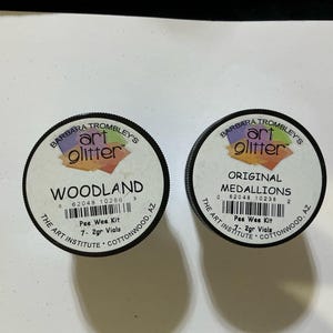 May include: A white ceramic mug with a black handle and the text "But First, Coffee" in a bold, black font. The mug is set against a blurred background, highlighting its clean design.