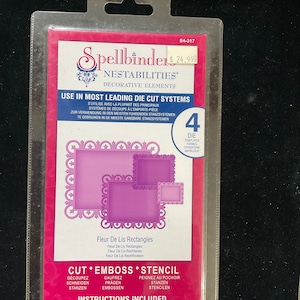 May include: A Spellbinders die set for crafting, featuring four rectangular frames with intricate floral designs. The set is labeled "Nestabilities Decorative Elements" and includes instructions for cutting, embossing, and stenciling. The die set is packaged in a clear plastic sleeve with a pink and white background.