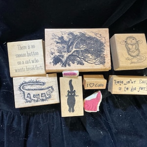May include: A collection of wooden rubber stamps featuring various cat-themed designs and text. The stamps include phrases like There is no snooze button on a cat who wants breakfast, I love Cats, and Hope your Easter is to dye for, with illustrations.