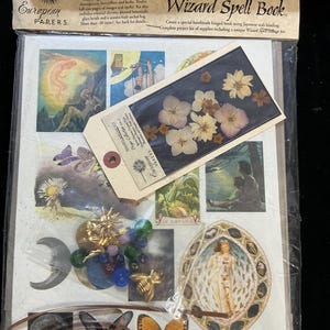 May include: A craft kit for making a Wizard Spell Book. The kit includes a variety of items, including dried flowers, paper, beads, and a charm. The kit is packaged in a clear plastic bag with a brown paper backing. The text on the packaging reads "Project Kit Wizard Spell Book".