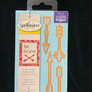 May include: A package of four gold-colored metal die-cut stencils featuring ornate arrows. The package is blue and white with the text "Spellbinders" and "be brave" on it. The package is labeled "Ornate Arrows" and "Templates/Modales/Plantillas".