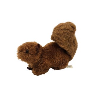 May include: A plush brown squirrel toy with a fluffy tail, small black eyes, and a small tag. The stuffed animal is made of soft, textured material and is positioned on a white background.