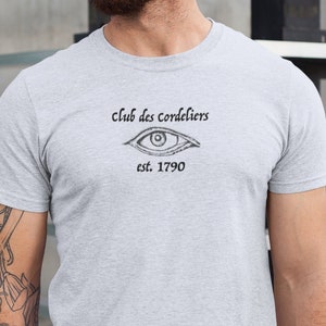 May include: A gray t-shirt with a black and white illustration of an eye and the text "Club des Cordeliers est. 1790".