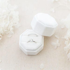May include: White velvet ring box with two silver rings inside. The box is octagonal and has a lid. The rings are a simple band and a solitaire engagement ring.