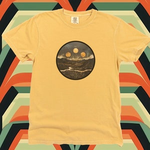 May include: A yellow t-shirt with a circular graphic of a mountain range with three moons in the sky.