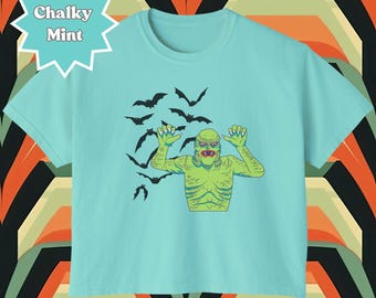 May include: A light blue t-shirt with a graphic print of a green monster with bats flying around it. The text "Chalky Mint" is on a starburst in the top left corner.