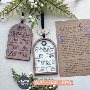 Op de afbeelding: Houten ornamenten voor een cadeau-uitwisselingsspel. Eén ornament is donkerbruin, de andere is lichtbruin. Beide hebben de tekst "Roll the Dice Gift Exchange Game" en dobbelinstructies. Een kaart met instructies is ook inbegrepen.