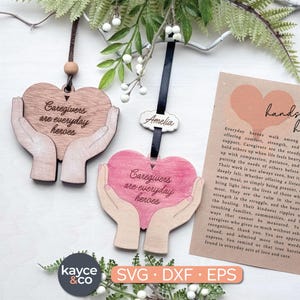 May include: Wooden heart-shaped ornaments with the phrase "Caregivers are everyday heroes" engraved on them. One is natural wood, the other is pink. Both feature hands cupping the heart. A card reads "hands that heal".