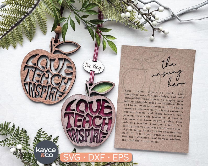 May include: Two wooden apple ornaments with the words "Love Teach Inspire" cut out. The ornaments are brown and burgundy. A card with the text "The Unsung Hero" and a message about teachers is in the background.