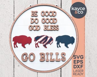 Puede incluir: Un letrero redondo de madera con fondo blanco y marco de madera marrón. El letrero presenta las palabras "BE GOOD, DO GOOD, GOD BLESS" y "GO BILLS" en letras marrones. También hay tres siluetas de búfalos.