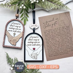 Puede incluir: Dos adornos de amistad de madera con el texto "Un amigo es la forma en que Dios se asegura de que nunca caminemos solos". Uno tiene una cruz, el otro un corazón rojo. También se muestra una tarjeta con un poema sobre la amistad.