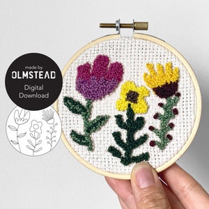 Puede incluir: Primer plano de una mano sosteniendo un pequeño aro de bordado con un diseño floral. El diseño presenta flores rosas, moradas, amarillas y verdes. El aro es de madera y tiene un fondo de tela blanca. El texto "made by OLMSTEAD Digital Download" es visible en la imagen.