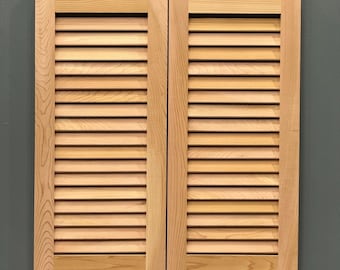 May include: A pair of wooden louvered shutters in a light brown color. The shutters are closed and have a rustic look.