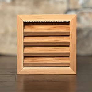 May include: A natural wood vent cover with a slatted design and a metal screen. The vent cover is a light brown color and has a square shape.