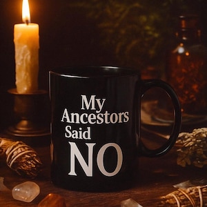 May include: A black ceramic mug with the text "My Ancestors Said NO" in white. A lit candle, crystals, and dried herbs are arranged around the mug on a wooden surface, creating a mystical aesthetic.